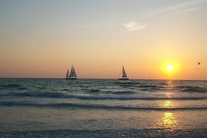 Um pôr do sol sobre o oceano com dois veleiros.