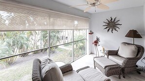 A room with a ceiling fan, large windows, wicker furniture, and a sun decoration on the wall. - Walk to Siesta Key Beach and Village - Beautifully Renovated 2BR Condo (Siesta Key)