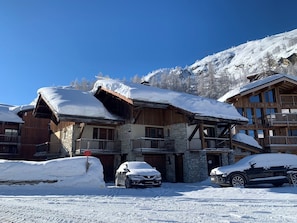 Eine Holzhütte mit Steinwänden und einem Balkon, ein Auto unter Schnee.