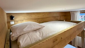 Una cama litera con cabecera de madera, una lámpara fijada a la pared y un enchufe.