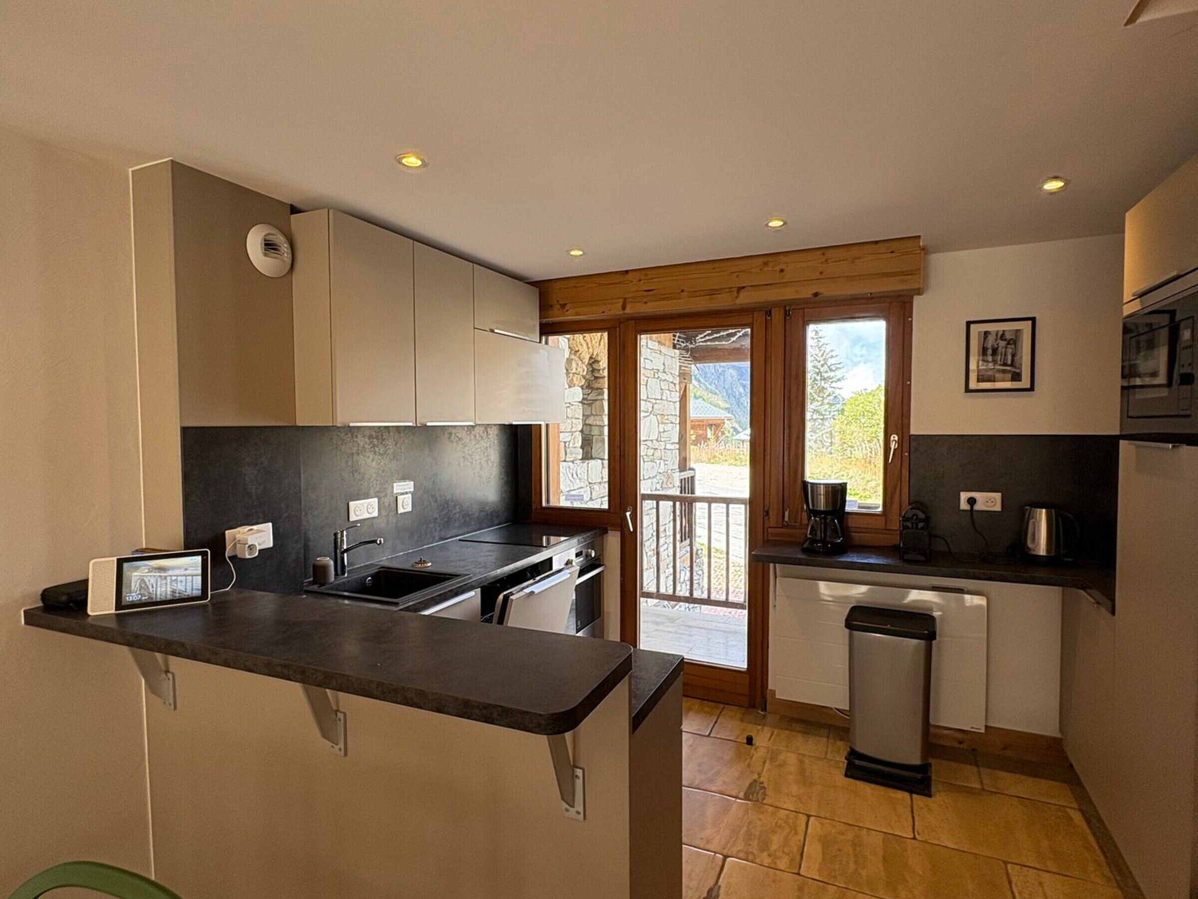 A modern kitchen with a built-in oven, a sink, and a coffee maker. There is a window with a view of the outside.