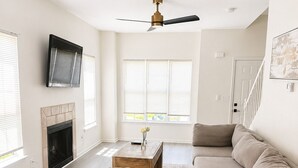 Uma sala de estar moderna com sofá seccional, lareira, ventilador de teto e TV na parede.