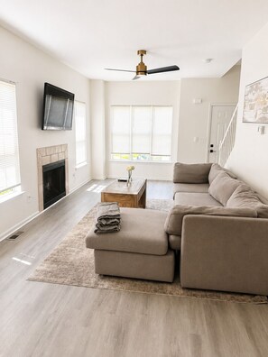 A modern living room with a sectional sofa, a fireplace, a ceiling fan, and a TV mounted on the wall. - Cozy 2-bedroom house in charming Atlanta (Atlanta)
