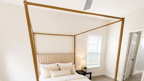 Uma cama de dossel com cabeceira, mesa de cabeceira, luminária e janela com persianas.