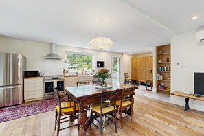 A modern kitchen with a dining area, wooden cabinets, and a large window.