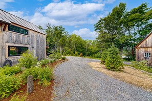 A rustic wooden building with a gravel driveway leading to a forested area.