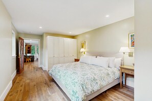 A bedroom with a bed, bedside table, lamp, wardrobe, and a view into another room.