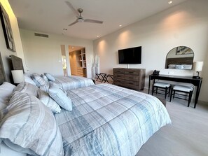 Ein Schlafzimmer mit einem großen Bett, einem Schreibtisch, einem Stuhl, einem Fernseher und einem Deckenventilator.