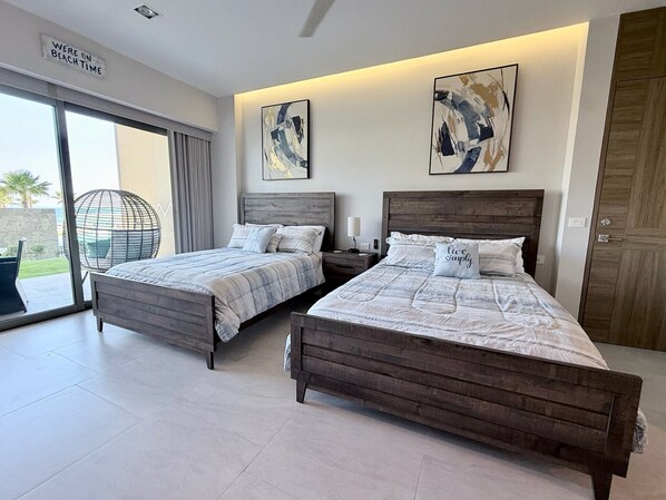 A modern bedroom with two wooden beds, a large window with a view, and abstract art on the walls. - Enjoy this new luxurious ground floor 3 bed condo in the heart of Rocky Point! (Puerto Peñasco)