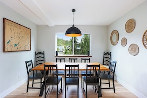 A dining area with a wooden table and chairs, a pendant light, a large window with a view, and decorative wall art. - Ski Bunny Betsy's Chalet | Family  and  Pet-Friendly Mountain Retreat  | Hot Tub | Mountain Views | 5 Minutes to the Lifts (Mount Washington)