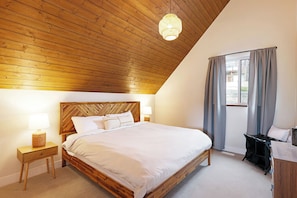 A bedroom with a wooden ceiling, a bed with white bedding, a nightstand with a lamp, and a window with curtains. - Ski Bunny Betsy's Chalet | Family  and  Pet-Friendly Mountain Retreat  | Hot Tub | Mountain Views | 5 Minutes to the Lifts (Mount Washington)