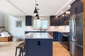 A modern kitchen with dark cabinetry, a central island, stainless steel appliances, and pendant lighting. - Ski Bunny Betsy's Chalet | Family  and  Pet-Friendly Mountain Retreat  | Hot Tub | Mountain Views | 5 Minutes to the Lifts (Mount Washington)