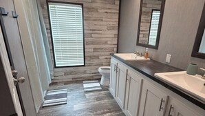 A modern bathroom with a wood-textured wall, a large mirror, a sink, and a toilet. - Countryside Home (Rayville)