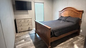 A bedroom with a wooden bed, a dresser, a television mounted on the wall, and a window with blinds. - Countryside Home (Rayville)