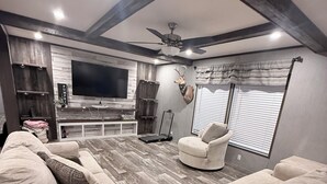 A modern living room with a large flat-screen TV, a ceiling fan, and a mounted deer head on the wall. - Countryside Home (Rayville)