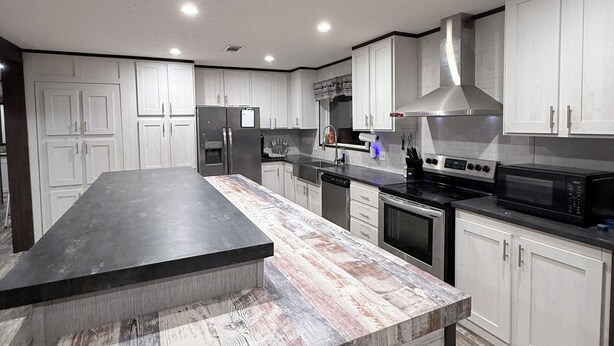 A modern kitchen with a central island, stainless steel appliances, and white cabinetry. - Countryside Home (Rayville)