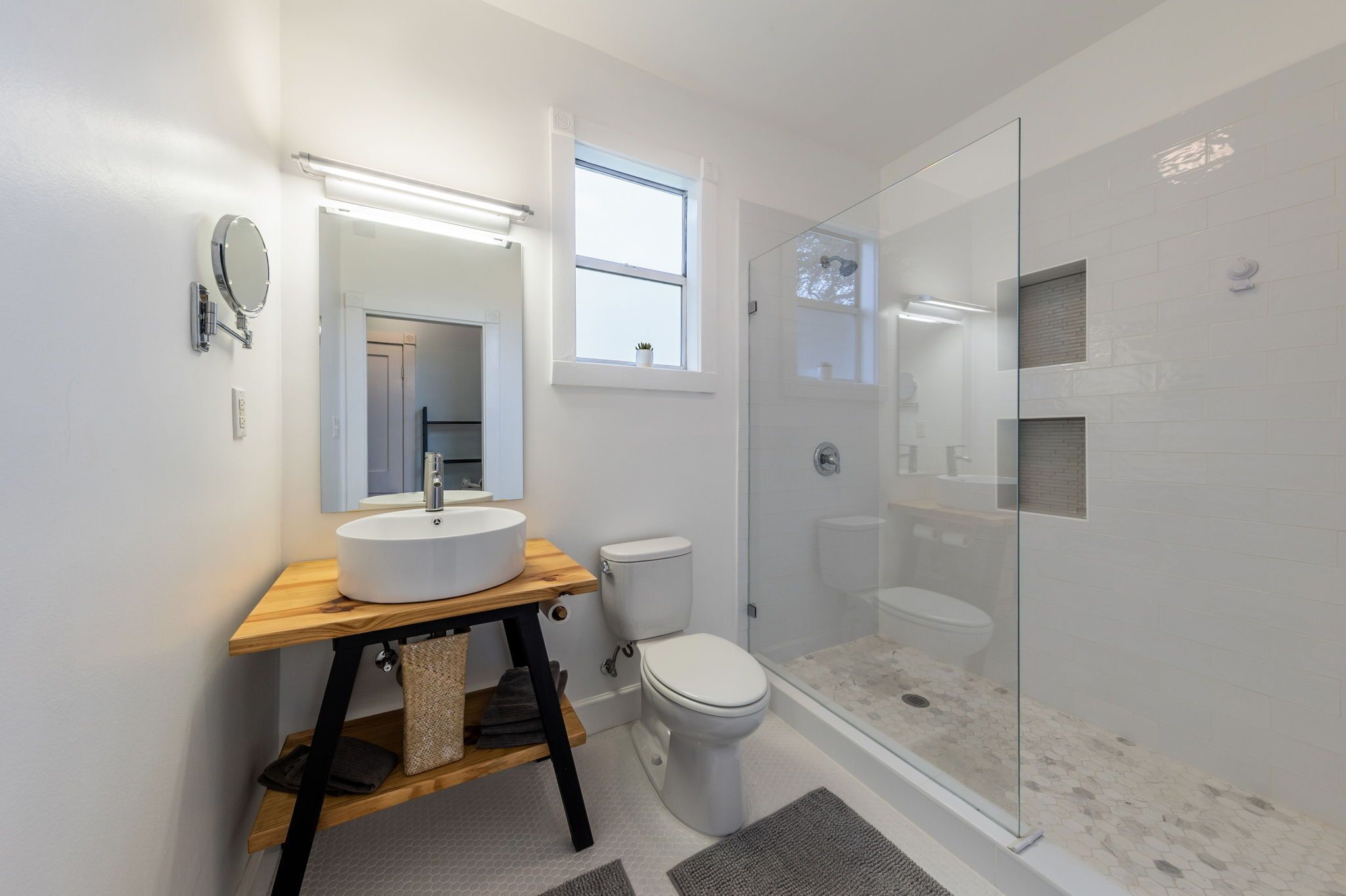 Une salle de bain moderne avec un meuble-lavabo en bois, un miroir rond, des toilettes et une douche à parois de verre.