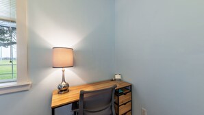 A corner room with a desk, chair, lamp, and a window.