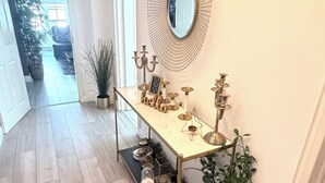 A hallway with a long table displaying various decorative items, a round mirror on the wall, and a potted plant. - Apartment Sleeps 11 with Air Conditioning (London)