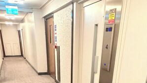 A hotel corridor with patterned carpet, a fire exit sign, a caution sign, and an elevator with the number 4. - Apartment Sleeps 11 with Air Conditioning (London)
