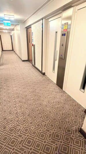 A hotel corridor with patterned carpet, a fire exit sign, a caution sign, and an elevator with the number 4. - Apartment Sleeps 11 with Air Conditioning (London)