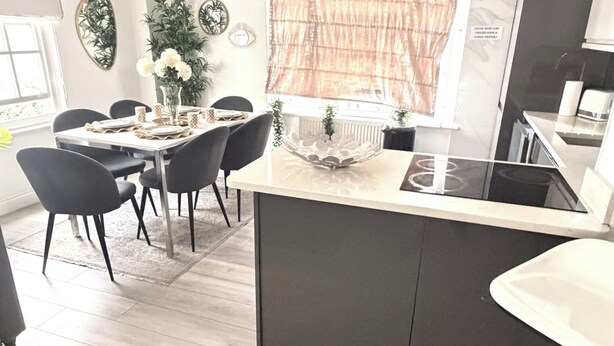 A modern kitchen with a central island, dining area with chairs, and a bar area with a stool. - Apartment Sleeps 11 with Air Conditioning (London)