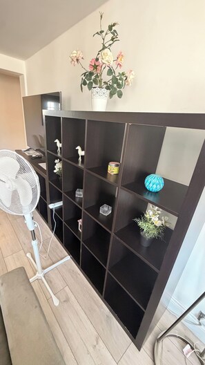 Ein Zimmer mit einer dunklen Holzregalanlage, einem weißen Ventilator und einer Wandvase mit Blumen.