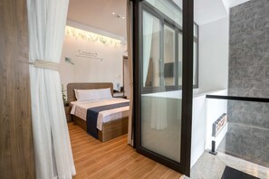 A modern bedroom with a bed, a nightstand, a wall-mounted lamp, and a view of the outside through a glass door. - Bin Bin Hotel 19 - Near Saigon Riverside (Ho Chi Minh City)