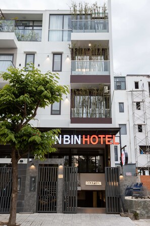 A modern hotel with a reception area, a tree in front, and a sign indicating the name 'BIN HOTEL'.