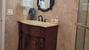 Une salle de bain avec un mur recouvert de carreaux de marbre, un meuble-lavabo en bois avec un évier, un miroir et une cabine de douche en verre.