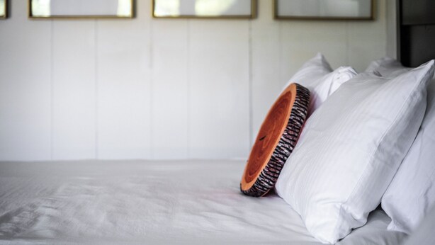 A bed with white linens, a wooden headboard, and a single white pillow. - Lumber Jill Lodge Rooms (Balsam Lake)