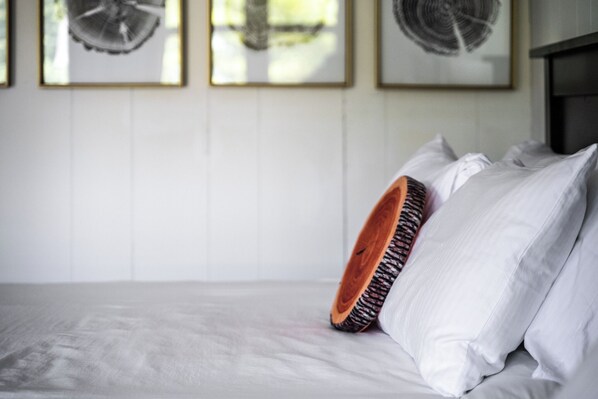 A bed with white linens, a wooden headboard, and a single white pillow.