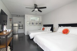 Quarto de hotel com duas camas, ventoinha no teto, geladeira, escrivaninha com cadeira e espelho.