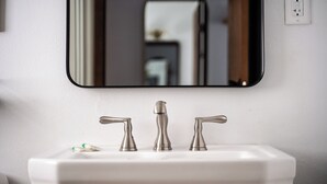Un baño con un lavamanos blanco, tres grifos y un espejo encima.