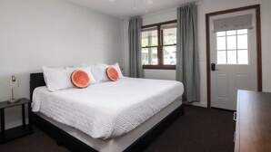 Un dormitorio con cama, mesita de noche, escritorio, ventilador de techo, ventana con cortinas y puerta.
