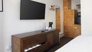 Habitación de hotel con cama, cómoda de madera, televisor de pantalla plana montado en la pared, armario de madera y microondas encima del armario.