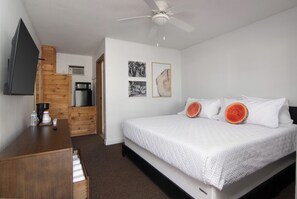 A bedroom with a bed, a desk, a television, and a ceiling fan.