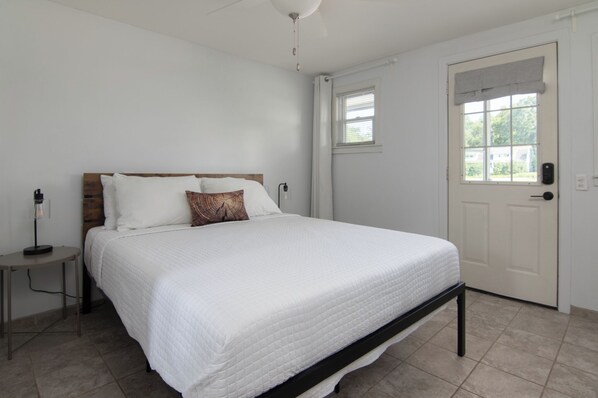 A bedroom with a bed, a bedside table, a lamp, a door, and a window.