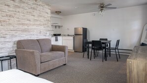 A compact room with a sofa, a dining table with chairs, a kitchenette, and a ceiling fan. - Lumber Jill Lodge Rooms (Balsam Lake)