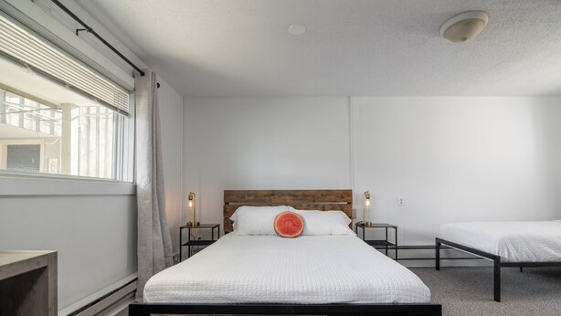A bedroom with a large bed, two bedside tables, a wooden headboard, a window with blinds, and a ceiling light. - Lumber Jill Lodge Rooms (Balsam Lake)