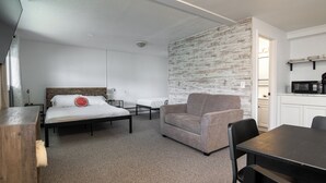 A compact room with a bed, a sofa, a dining table, and a kitchenette. - Lumber Jill Lodge Rooms (Balsam Lake)