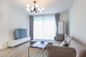 Una sala de estar moderna con un televisor de pantalla plana, un sofá, una mesa de centro y una lámpara de techo.