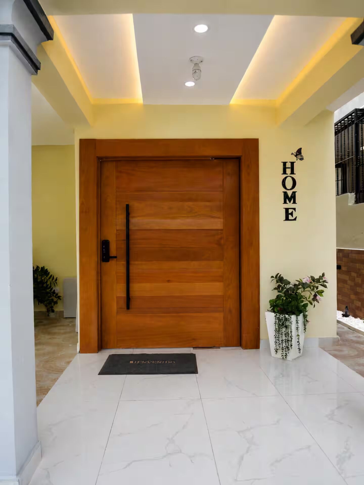 A wooden door with a black handle, a 'HOME' sign on the wall, and a potted plant.