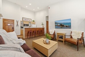 Ein Wohnzimmer mit einer Couch, einem Couchtisch, einem Fernseher und einer Küchenzeile mit Bar.