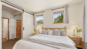 A bedroom with a large bed, two bedside tables with lamps, a window with a view, and a door leading to another room. - Mountain View Ski-In/Out Palisades Condo Hot-Tub (Olympic Valley)