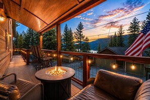 A wooden deck with a fire pit, seating, and a view of trees and mountains.