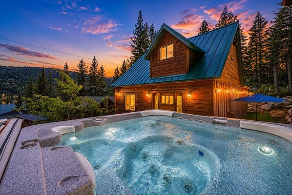 A wooden cabin with a hot tub and a mountain backdrop.