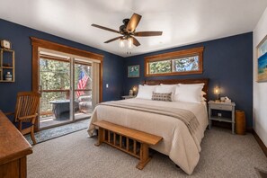 A bedroom with a bed, a ceiling fan, a nightstand, a bench, and a view of the outdoors.