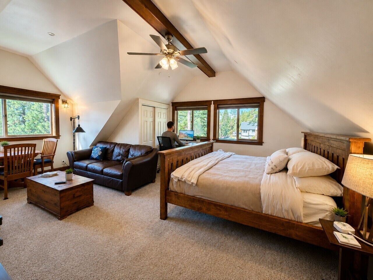 A bedroom with a sloped ceiling, a bed, a desk, a chair, and a couch.