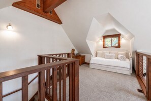 Ein Schlafzimmer mit schrägen Wänden, einem Bett, einem Nachttisch und einem Fenster mit Blick.